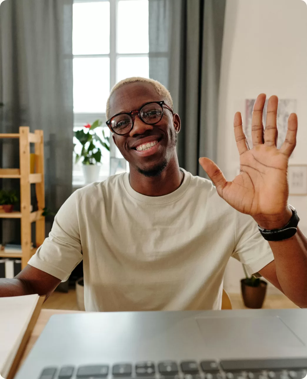 A smiling man waving hello over a laptop
