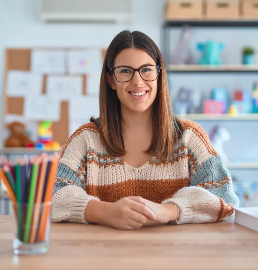 A teacher with glasses smiling at her desk